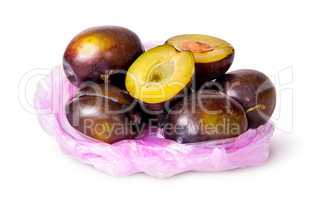 Whole and half violet plums in plastic bag