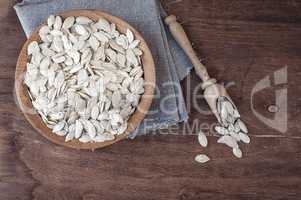 Unpeeled pumpkin seeds in a wooden bowl