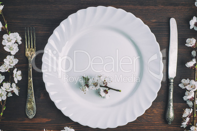 White plate with a fork and knife on a brown wooden surface