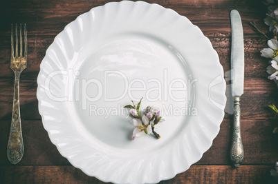 Empty plate with a fork and knife on a brown wooden surface