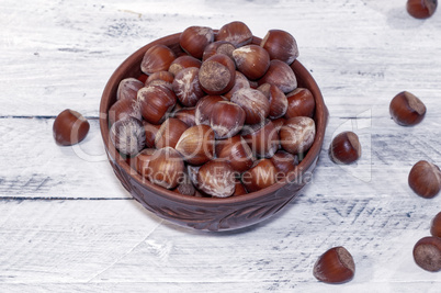 Hazelnuts in a shell in a clay bowl on a white surface