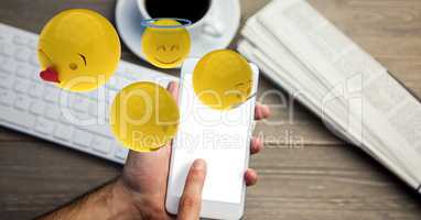 Digitally generated image of emojis flying over hands using smart phone with laptop on table