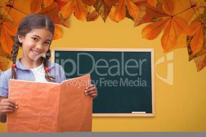 Female student holding book against chalkboard and leaves