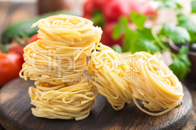 Raw all'uovo pasta, egg noodles with cooking ingredients on dark wooden rustic background, traditional italian cuisine