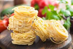 Raw all'uovo pasta, egg noodles with cooking ingredients on dark wooden rustic background, traditional italian cuisine