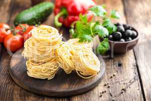 Raw all'uovo pasta, egg noodles with cooking ingredients on dark wooden rustic background, traditional italian cuisine