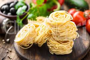 Raw all'uovo pasta, egg noodles with cooking ingredients on dark wooden rustic background, traditional italian cuisine