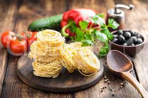 Raw all'uovo pasta, egg noodles with cooking ingredients on dark wooden rustic background, traditional italian cuisine