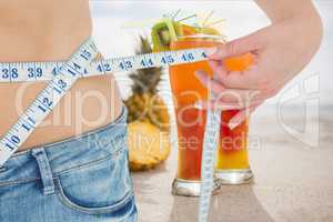 Midsection section of woman measuring waist with juices in background