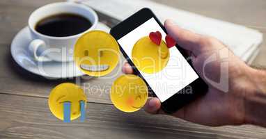 Close-up of hand using smart phone while emojis flying over table