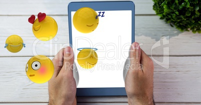 Close-up of hands holding digital tablet with various emojis at wooden table