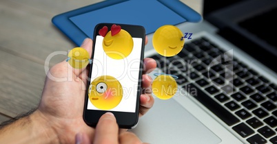 Close-up of hands holding mobile phone with various emojis at wooden table