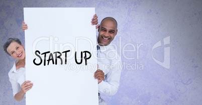 Portrait of smiling business people holding billboard with start up text against gray background