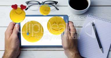 Hands holding digital tablet with emojis coming out