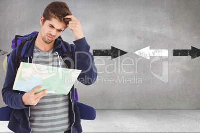 Confused male hiker reading map while standing against arrows in background