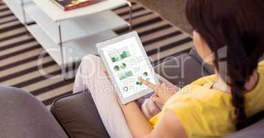 High angle view of woman analyzing charts on digital tablet while sitting on sofa