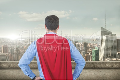 Businessman in super hero costume looking at cityscape