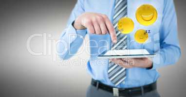 Business man mid section with tablet and emojis with flares against grey background