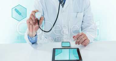 Midsection of doctor using stethoscope with digital tablet and mobile phone on desk