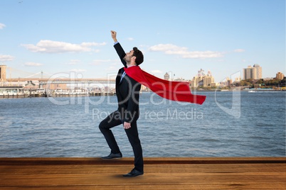 Side view of businessman wearing cape with arm raised standing by river against city