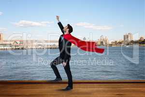 Side view of businessman wearing cape with arm raised standing by river against city