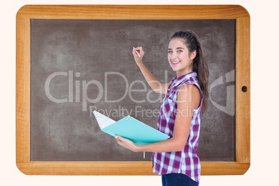 Side view of woman holding book while writing on blackboard