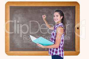 Side view of woman holding book while writing on blackboard