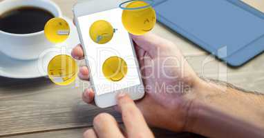 Digital composite image of hand using smart phone while emojis flying over table
