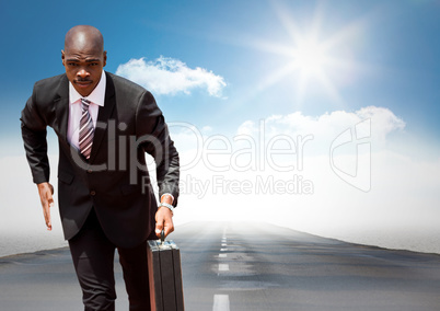 Business man running with briefcase on road against sky with sun
