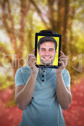 Composite image of man holding digital tablet in front of face