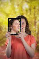 Composite image of beautiful woman holding digital tablet in front of her face