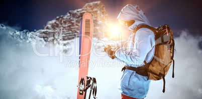 Composite image of skier with skis and backpack using mobile phone