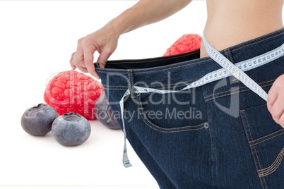 Midsetion of woman wearing loose jeans with fruits in background