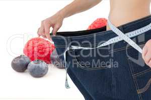 Midsetion of woman wearing loose jeans with fruits in background