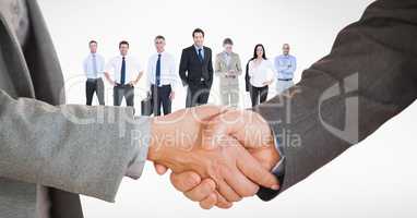 Cropped image of business people doing handshake with employees in background