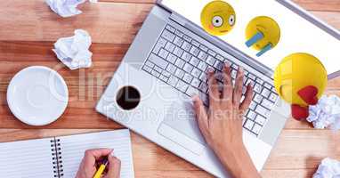 Emojis flying over hands writing in book while using laptop