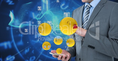 Digitally generated image of emojis flying by businessman using smart phone against tech graphics