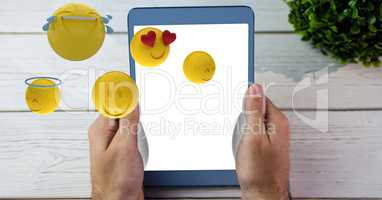 Hands holding tablet PC while emojis flying over table