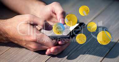 Digital composite image of hands using smart phone while emojis flying over table