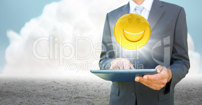 Business man mid section with tablet and emoji with flare against cloud and ground