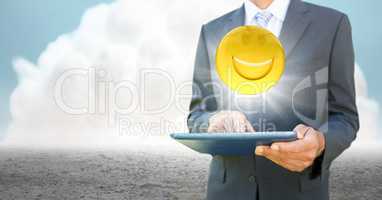 Business man mid section with tablet and emoji with flare against cloud and ground