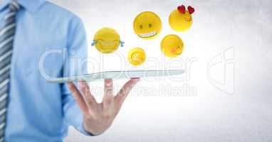 Business man mid section holding tablet with one hand and emojis against white wall