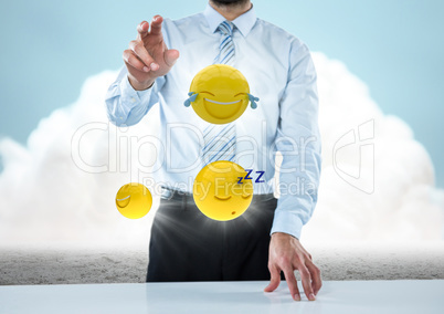 Business man at desk with emojis and flares against ground and cloud