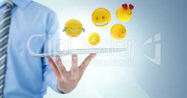 Business man mid section holding tablet with one hand and emojis against blue background