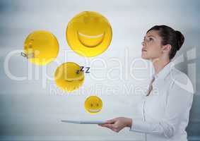 Business woman with tablet looking up at emojis against grey wood panel