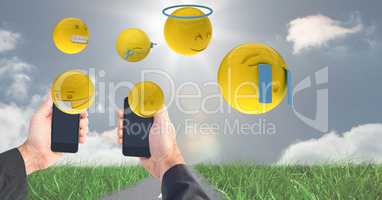 Digitally generated image of emojis flying over hands holding smart phone at field against sky