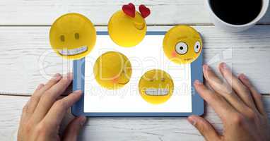 Close-up of hands using digital tablet with various emojis at wooden table