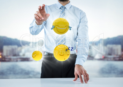 Business man at desk with emojis and flares against blurry skyline
