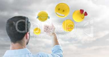Back of man holding up glass device against cloudy sky with emojis and flare