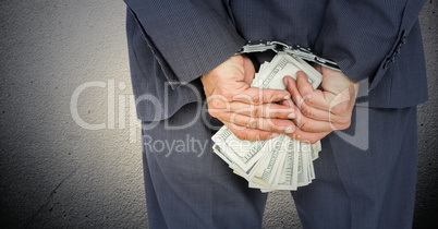 Close up of business man's hands behind back with money and handcuffs against white wall